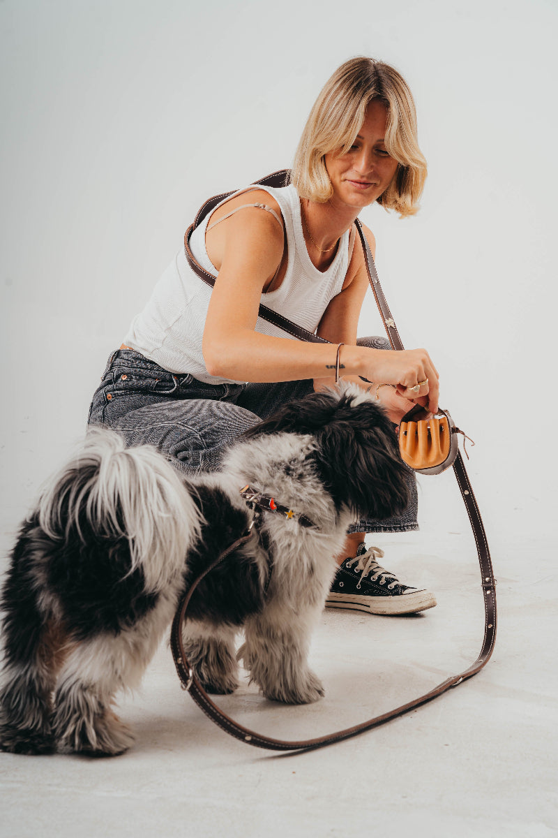 Woman with a small dog on a leash against a plain background wearing Mou Mou couture handcrafted pouch leash and harness