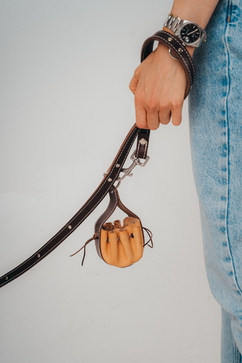 Hand holding a handmade leather dog pouch for sanitary bags or treats from Mou Mou Couture displayed on a white background