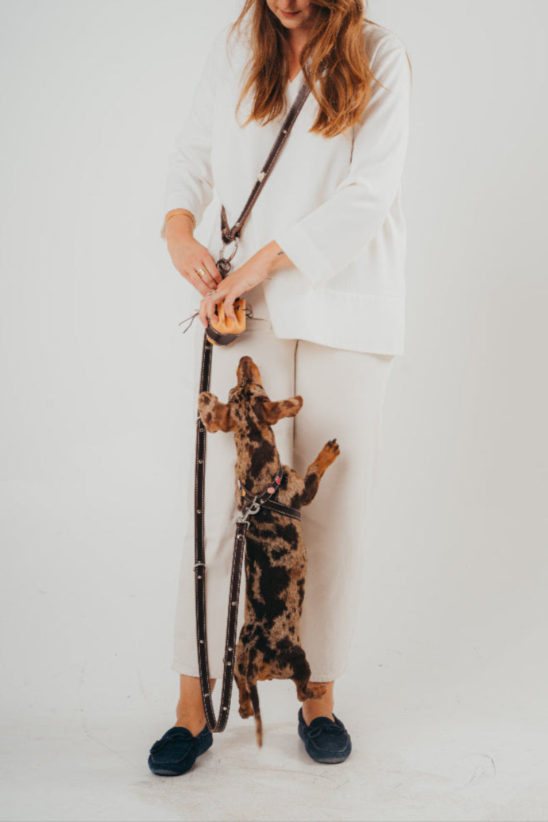 Handmade leather dog pouch for sanitary bags or treats from Mou Mou Couture displayed with a woman and a dachshund on a white background